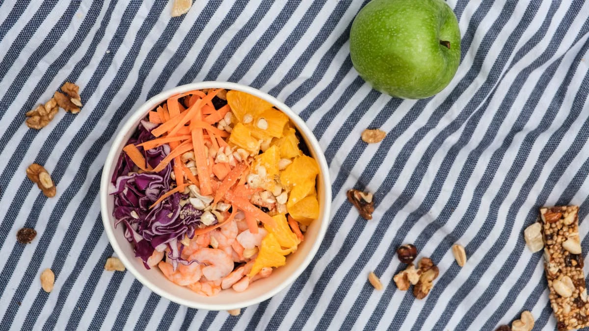Top view of fresh poke bowl near green apple and nuts on surface